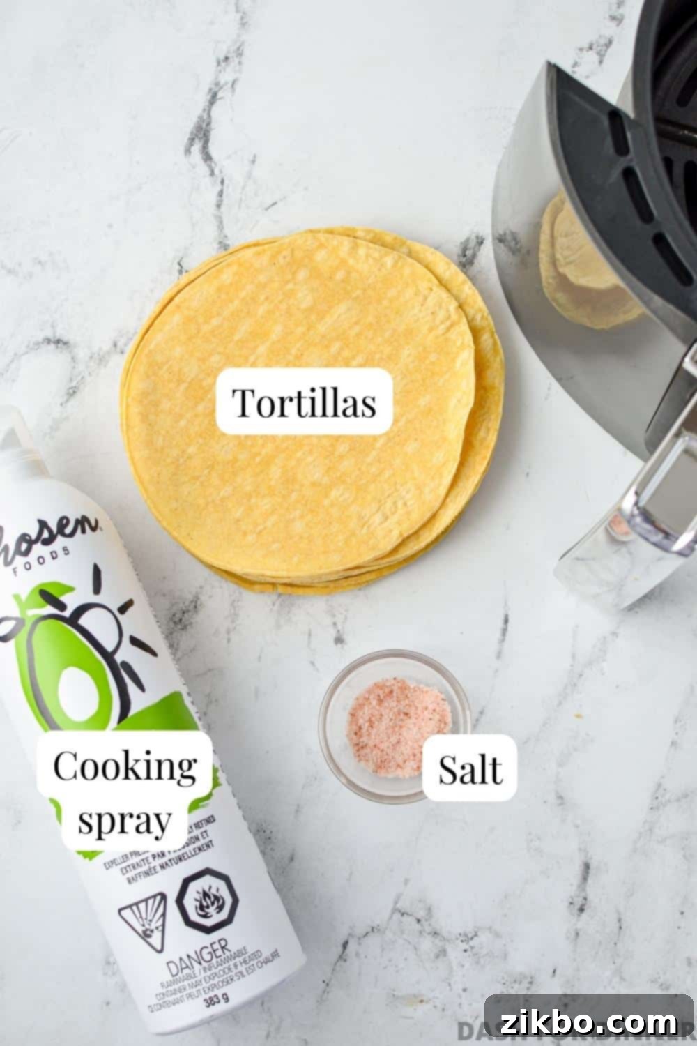 The simple ingredients needed to make air fryer tortilla chips: a stack of corn tortillas, a bottle of oil spray, and a small dish of salt.