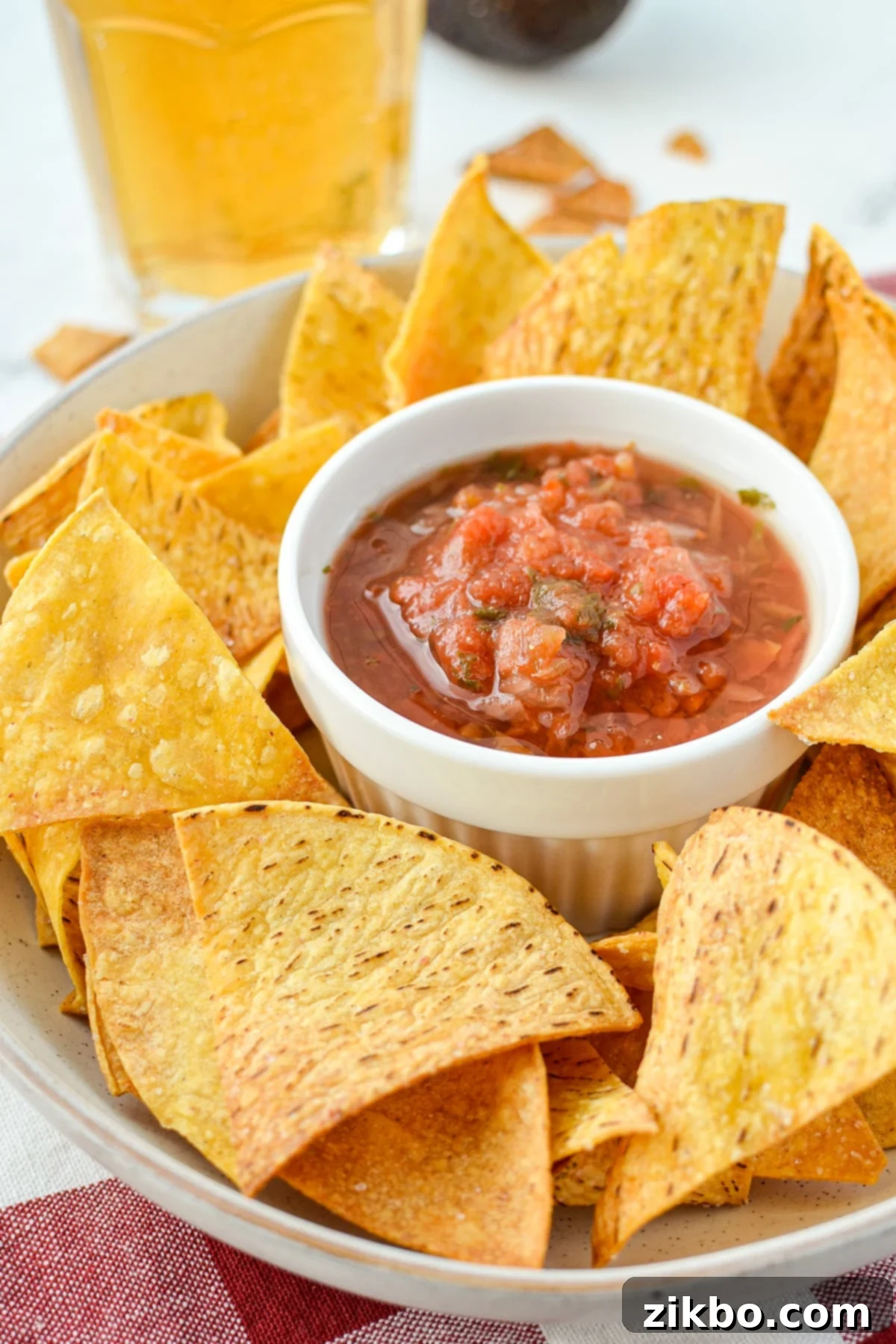 A rustic bowl filled with golden air fryer tortilla chips, with a small ceramic bowl of vibrant red salsa nestled in the center.