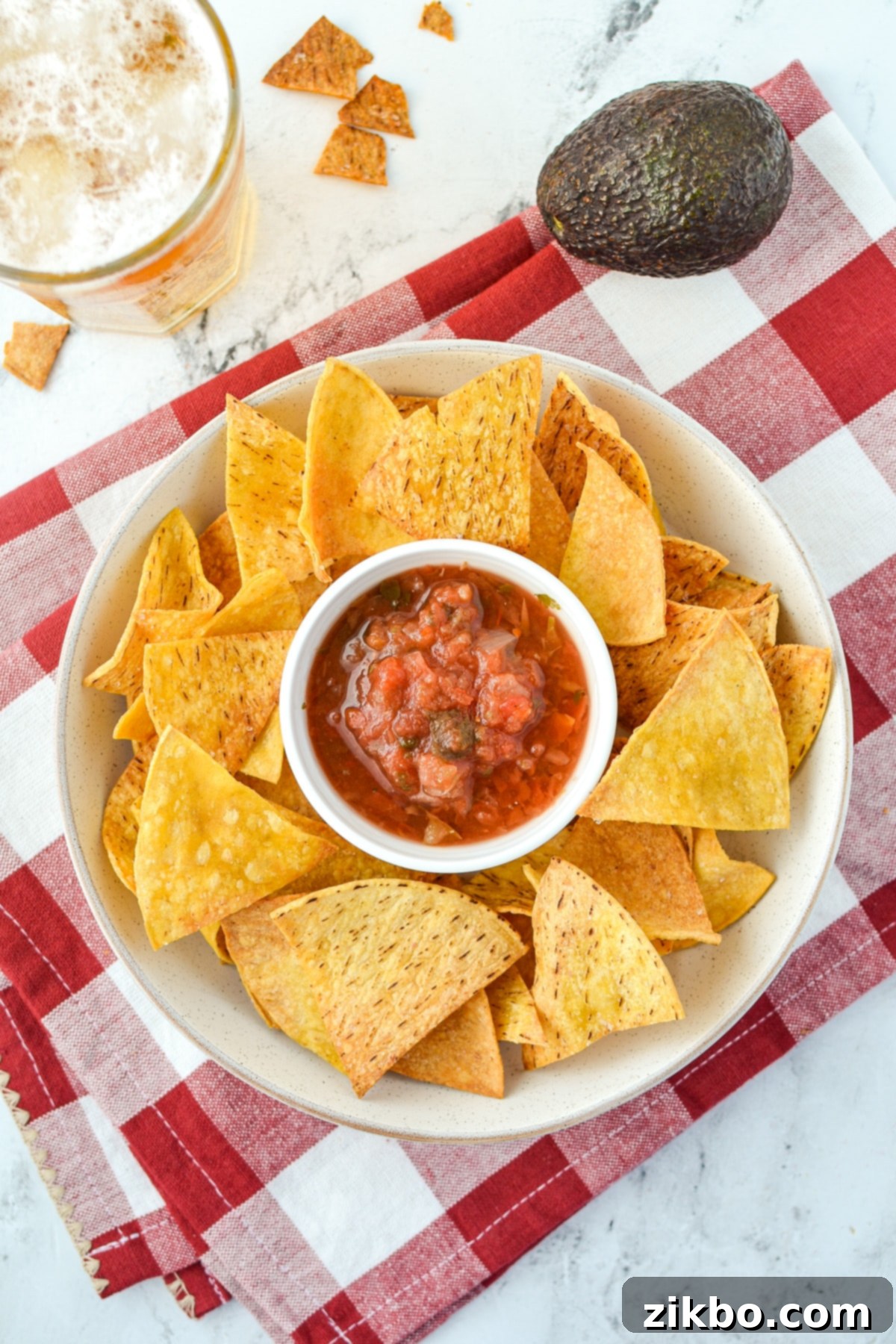 An overhead view of a circular plate of golden tortilla chips arranged around a small bowl of fresh salsa.