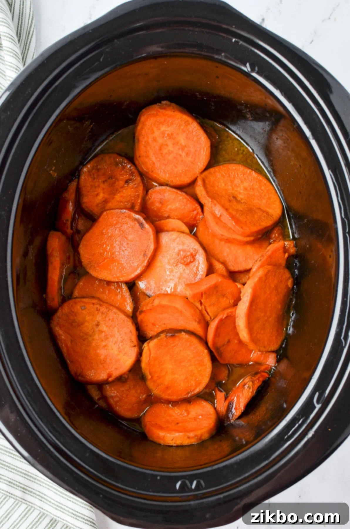 A slow cooker with sliced sweet potatoes in it.