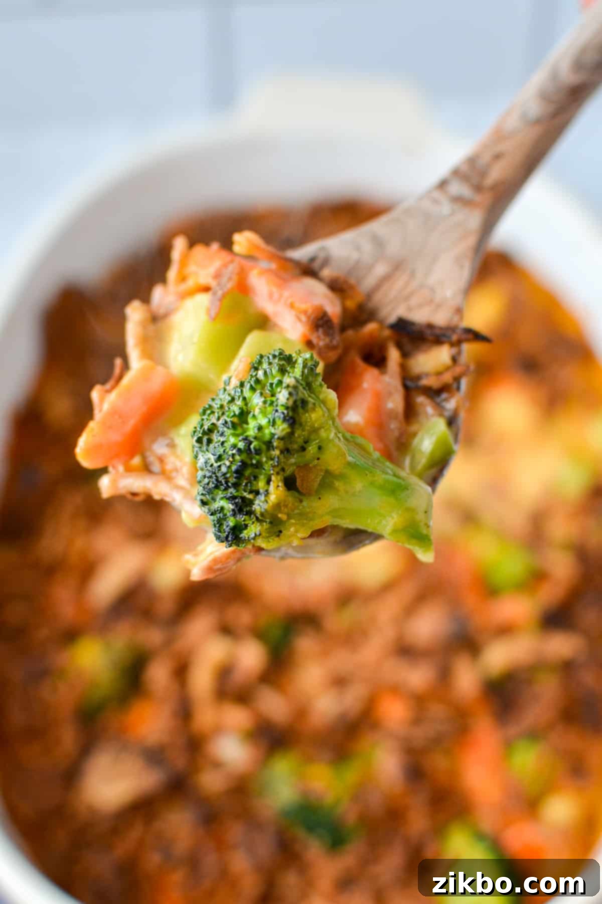 A wooden spoon scooping a portion of the creamy cheesy vegetable casserole, showing the texture and mix of vegetables.