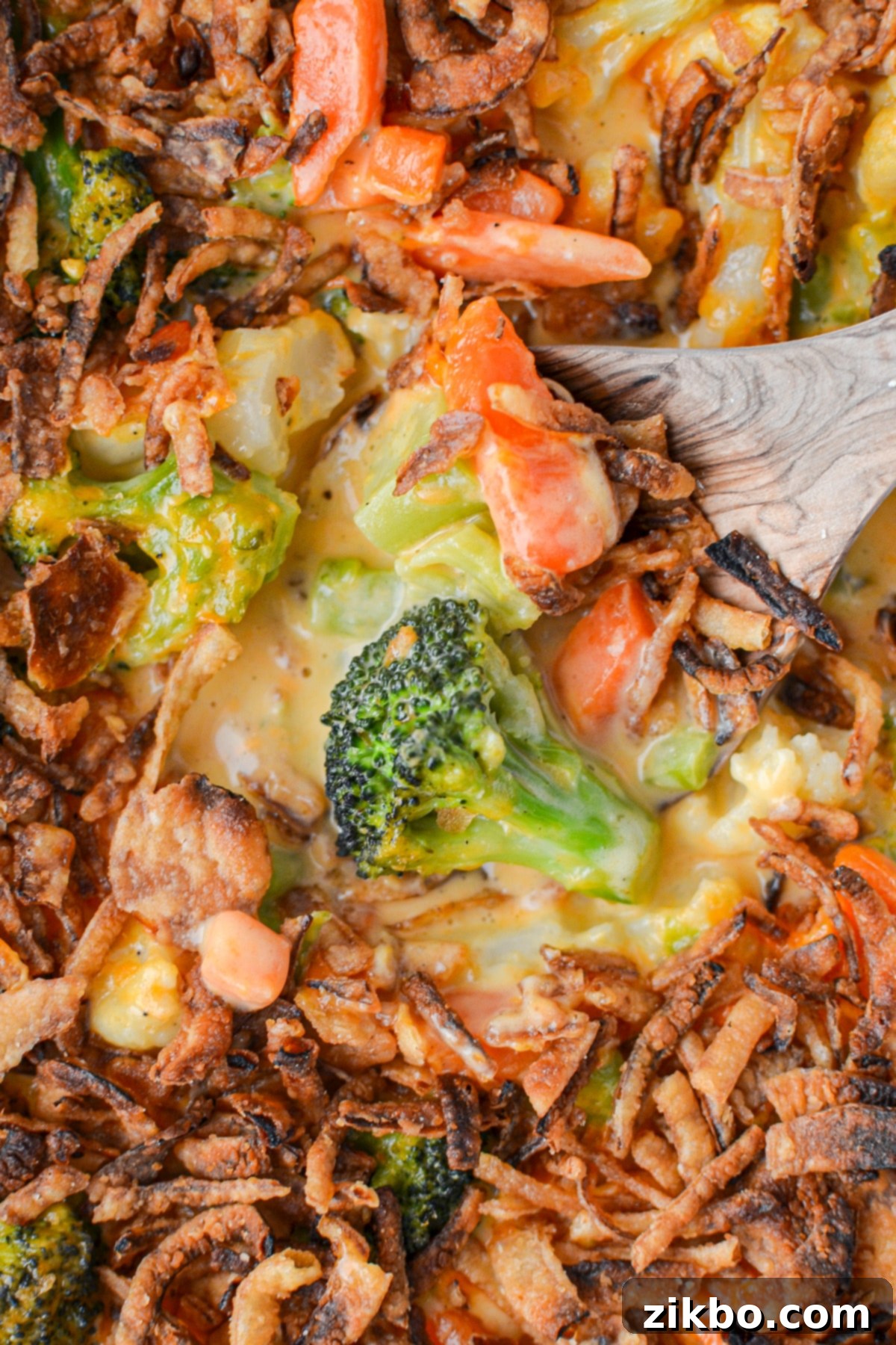 A wooden spoon scooping out a hearty portion of vegetable casserole, showcasing the cheesy sauce and visible broccoli florets.