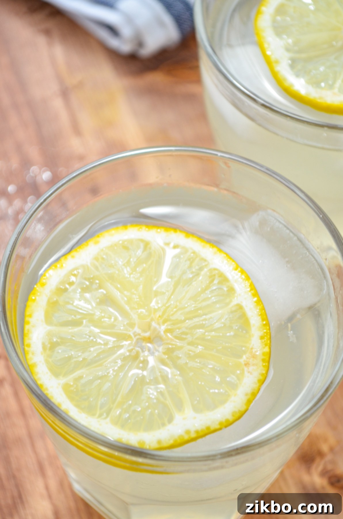 Two glasses of sparkling Instant Pot lemonade with fresh lemon and mint garnishes on a light wooden surface.