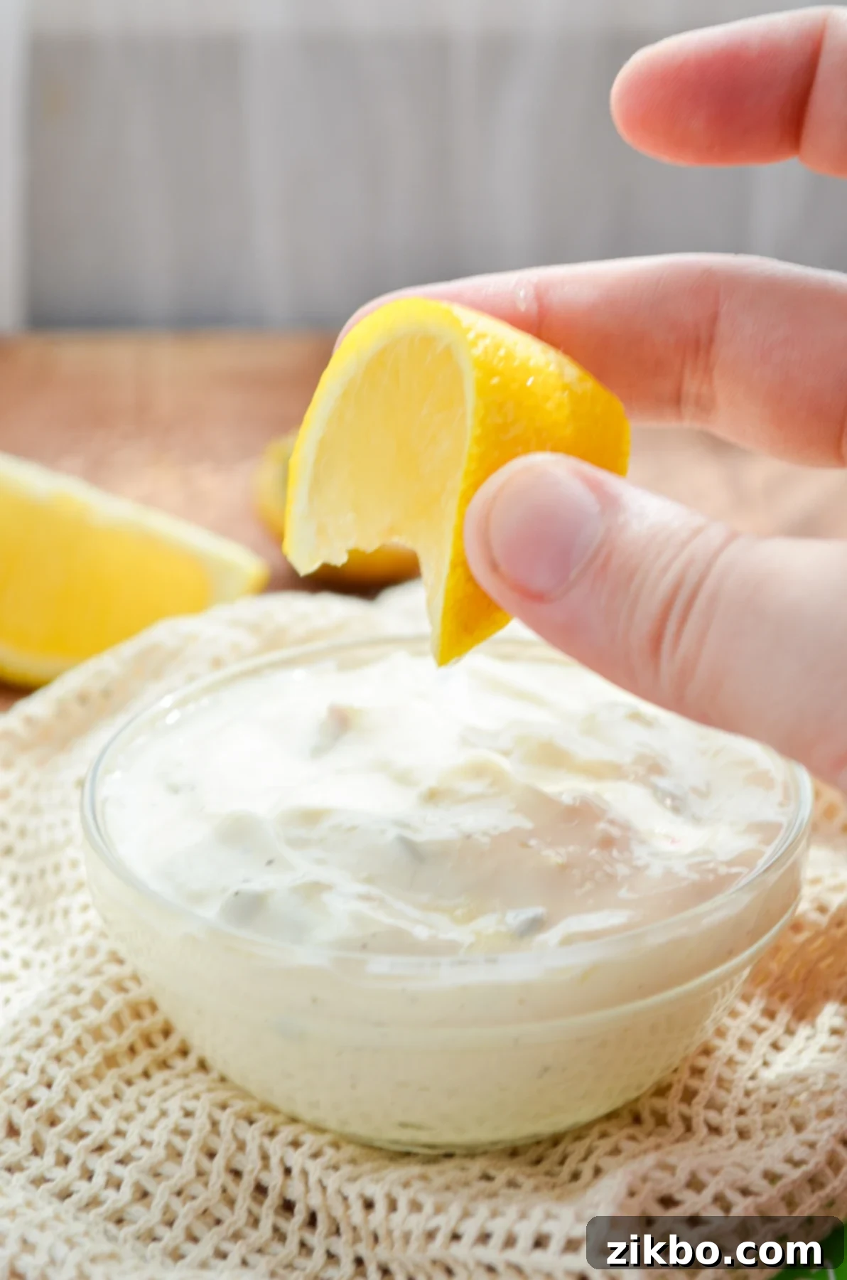 A small bowl of simple tartar sauce, with lemon being squeezed into it.