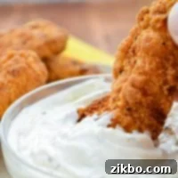 A fried chicken strip being dipped into ranch dip.