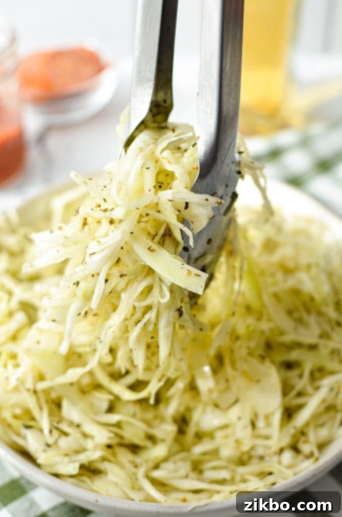 Tongs taking a portion of a coleslaw made with vinegar.