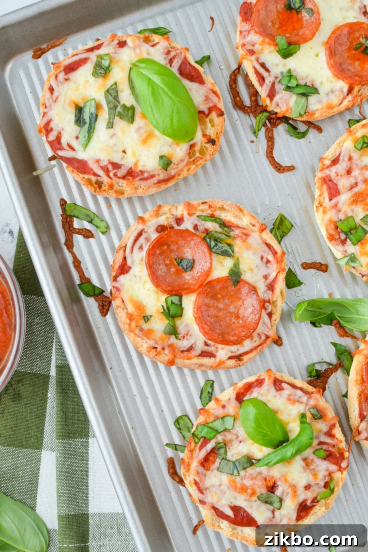 Easy English Muffin Pizzas 2 A baking sheet with English muffin pizzas topped with pepperoni and basil.