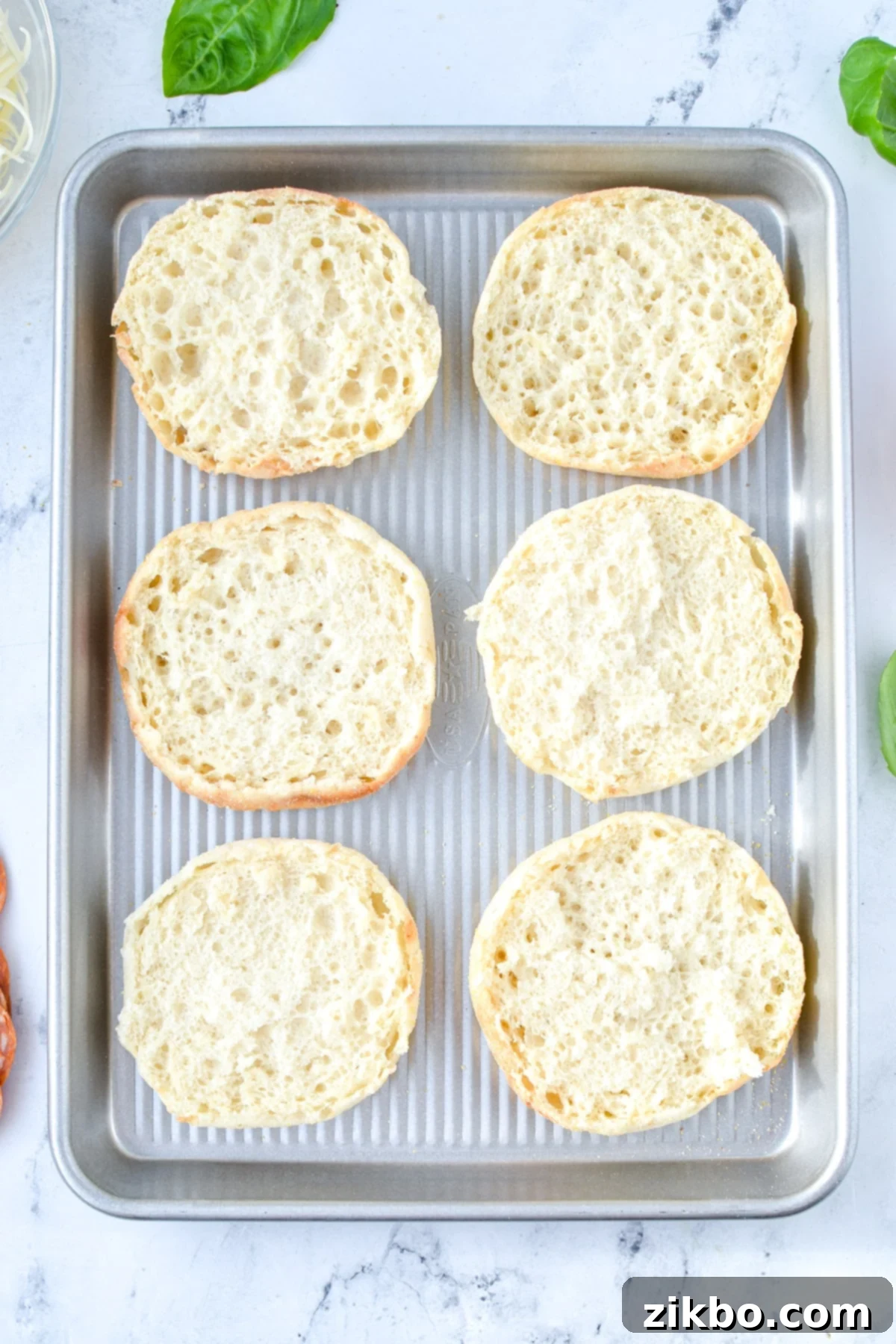 Easy English Muffin Pizzas 4 A baking sheet with English muffin halves on it.