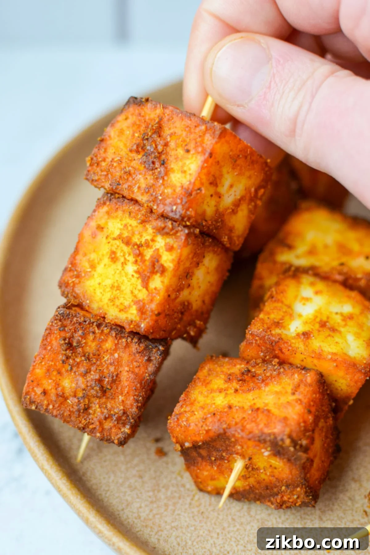 Quick Air Fryer Paneer 2 A hand holding a skewer filled with seasoned paneer cubes.