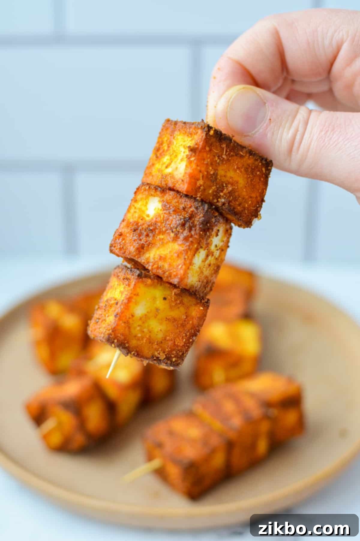 Quick Air Fryer Paneer 7 A hand holding a skewer with three cubes of seasoned paneer speared onto it.