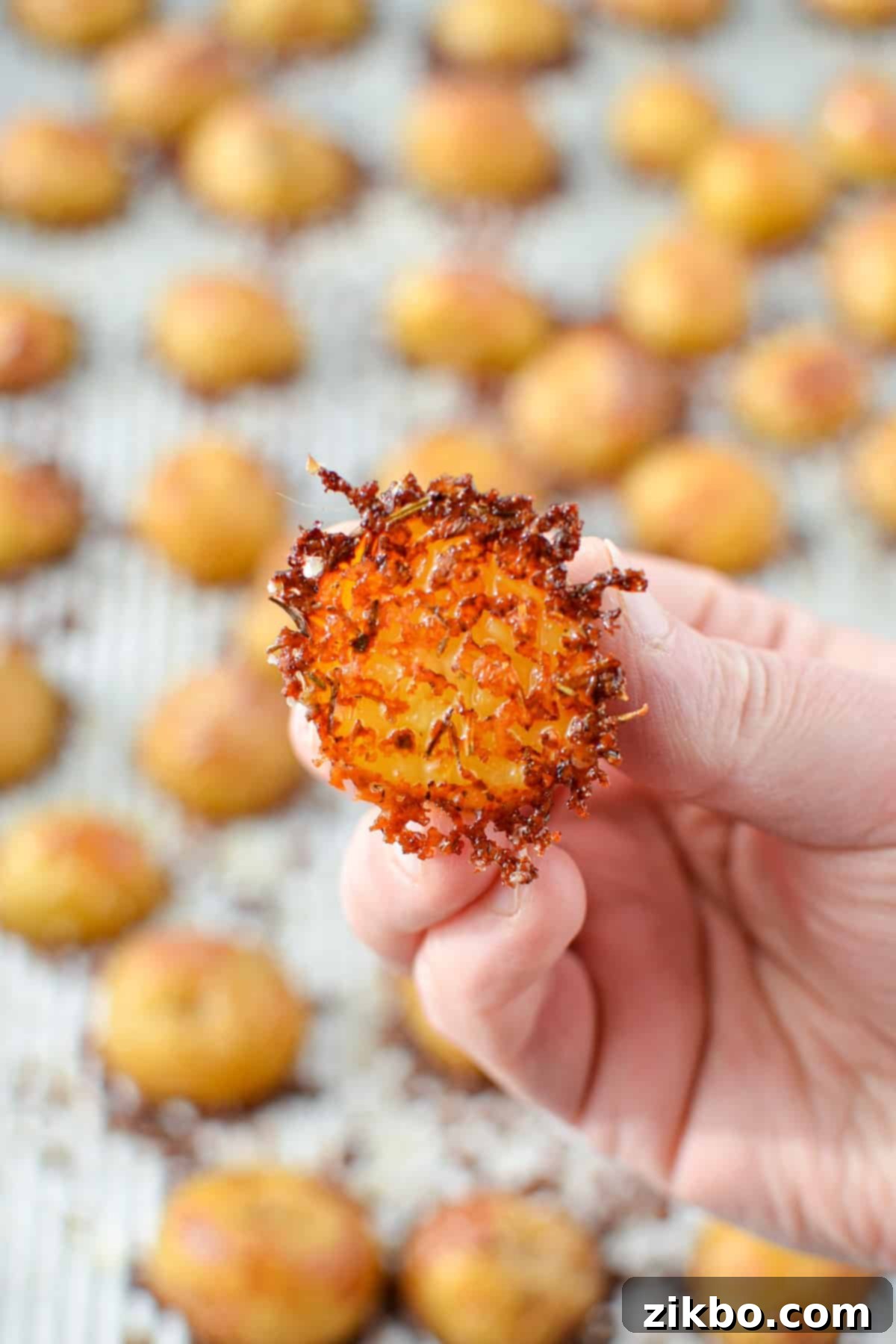 Crispy Parmesan Potatoes 8 A hand holding up a single, perfectly golden-brown parmesan encrusted potato, ready to be eaten.