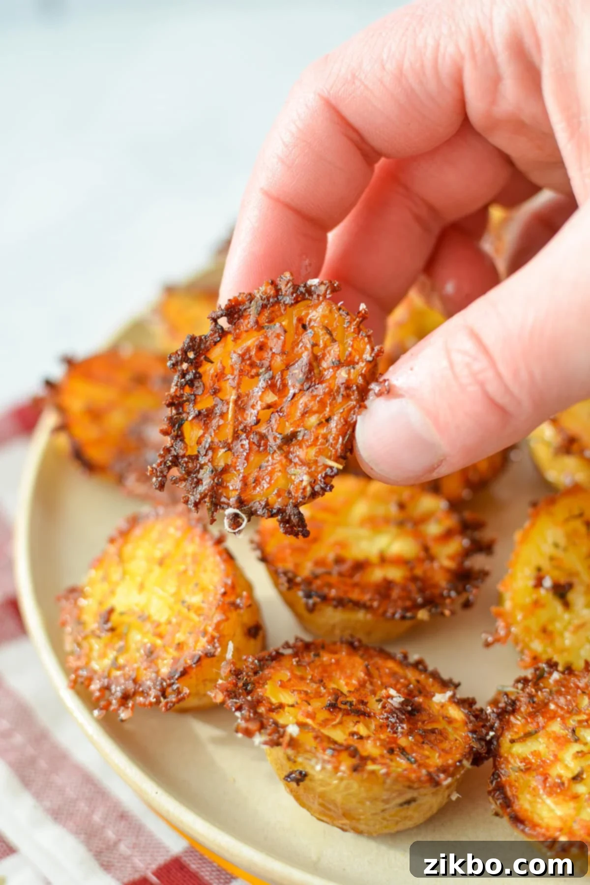 Crispy Parmesan Potatoes 9 A hand taking a small potato from a plate of roasted parmesan potatoes, demonstrating their irresistible appeal.