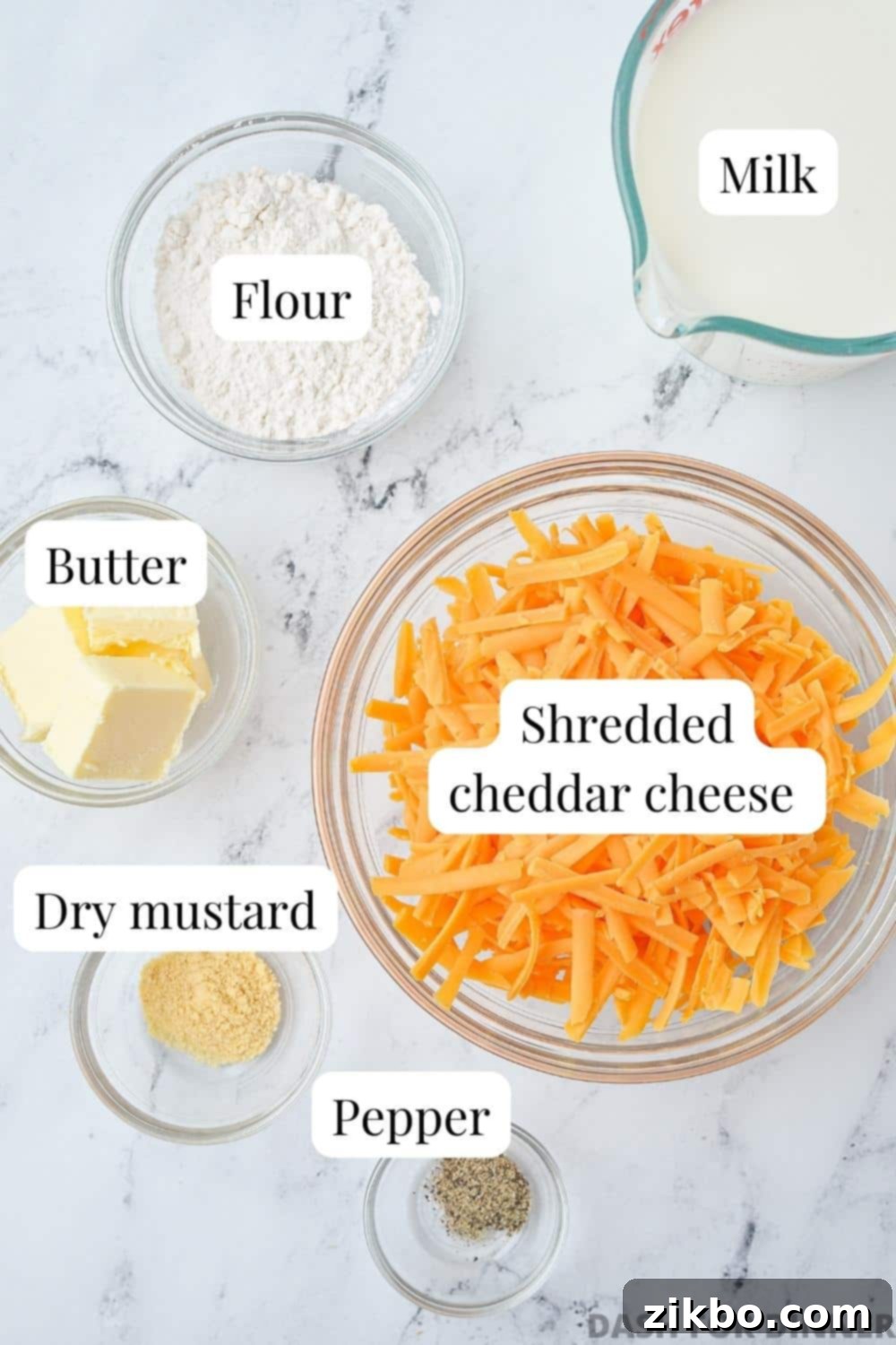The ingredients needed to make cheese sauce: shredded cheddar, butter, milk, flour, dry mustard, etc.