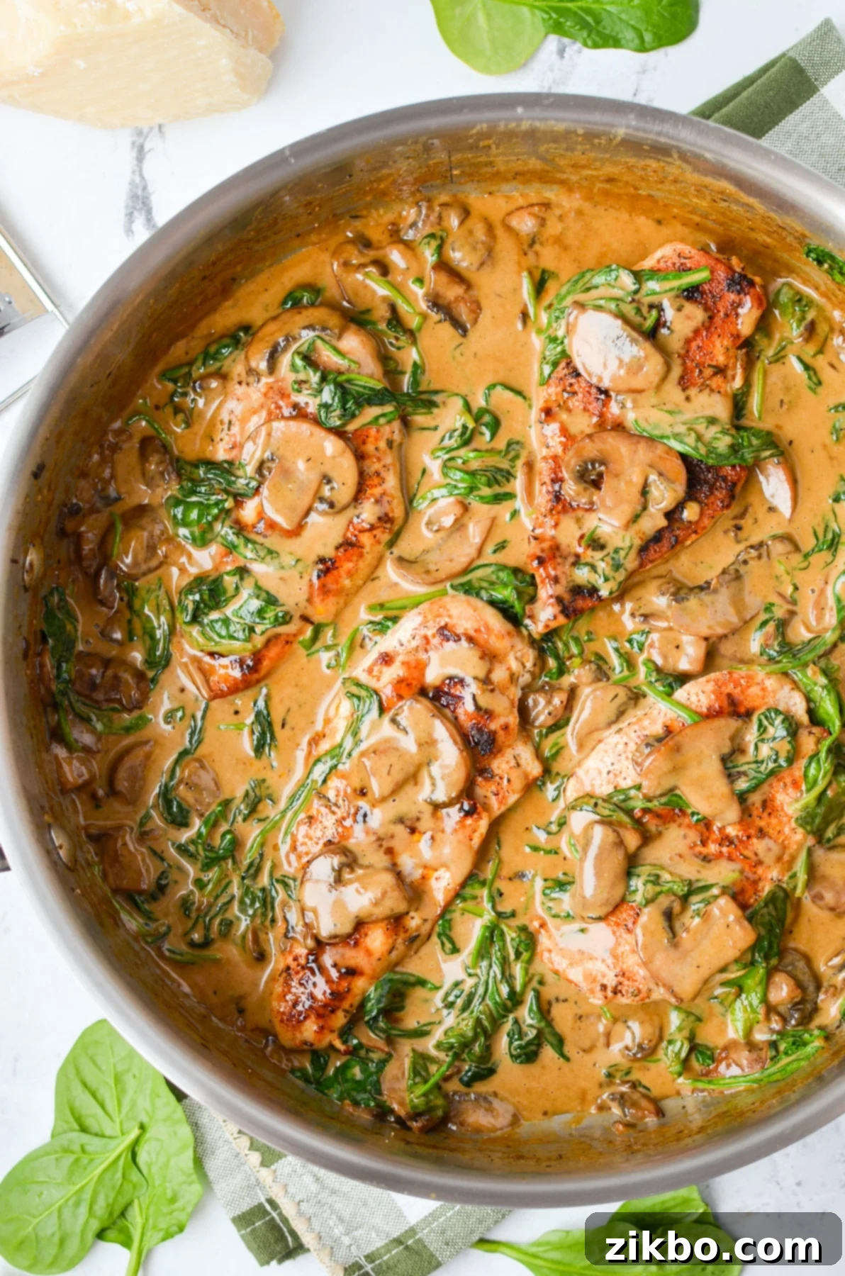 A skillet with chicken covered in a spinach and mushroom cream sauce.