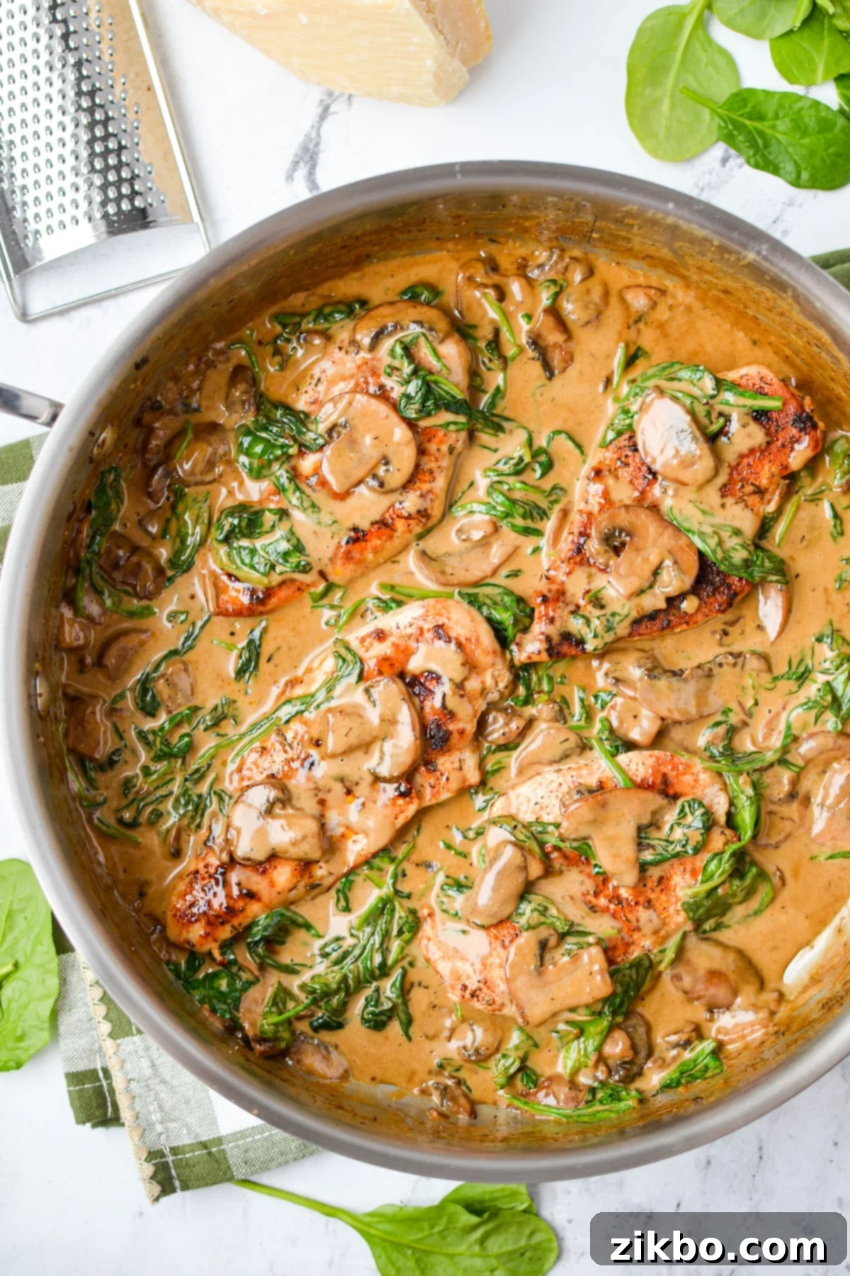 A skillet with chicken in cream sauce, with a chunk of parmesan on the side.