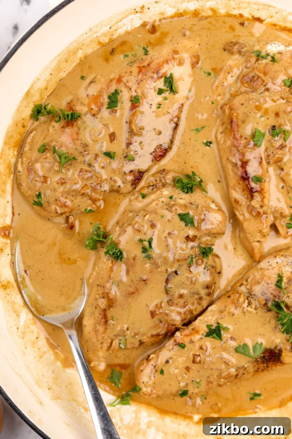 Four golden-brown chicken breasts nestled in a rich, creamy Diane sauce, with a spoonful of sauce on the side for garnish.