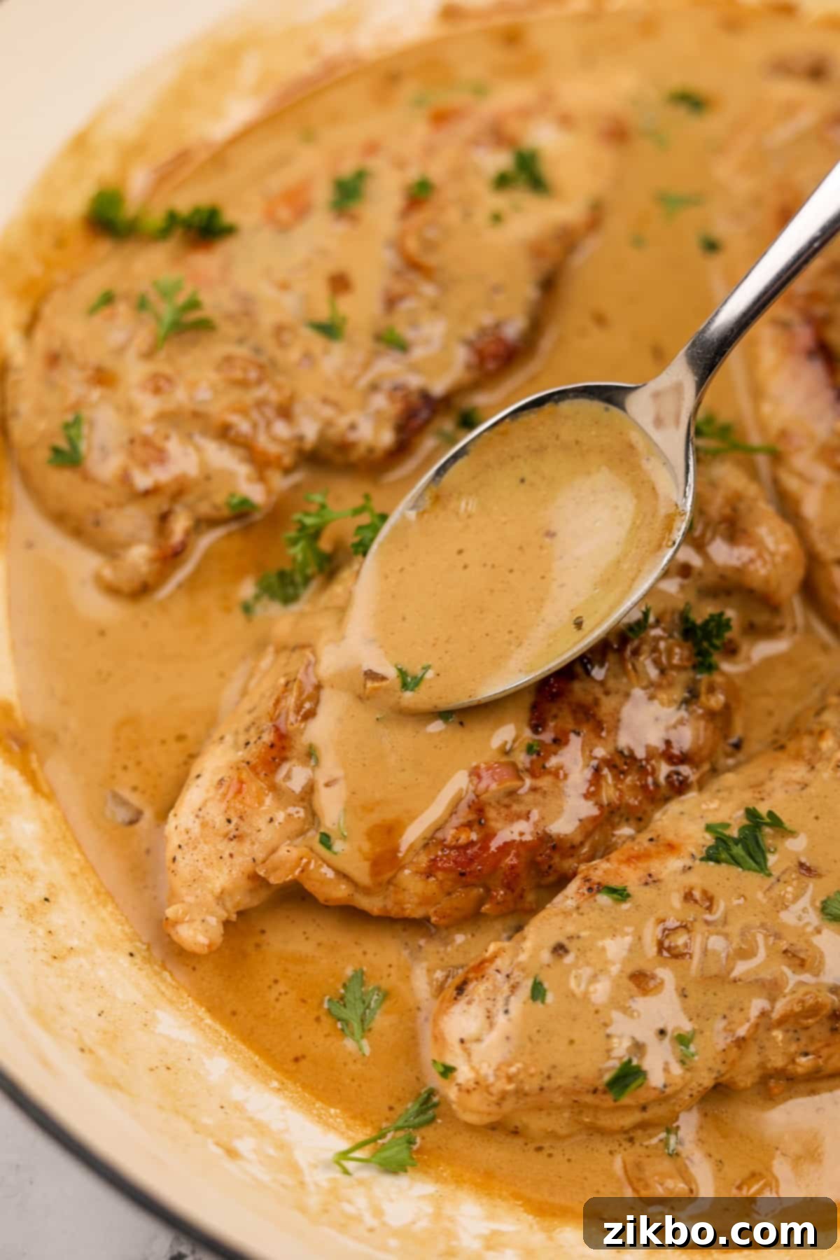 A hand spooning the creamy Diane sauce over a perfectly cooked chicken breast in a skillet, enhancing its presentation and flavor.