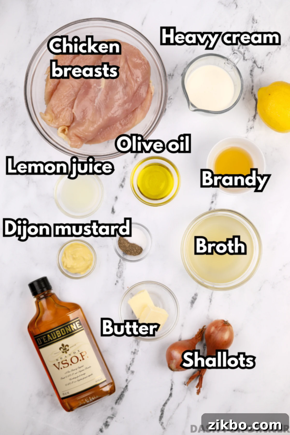 A selection of fresh ingredients including brandy, chicken broth, Dijon mustard, olive oil, and butter, laid out for making Chicken Diane.