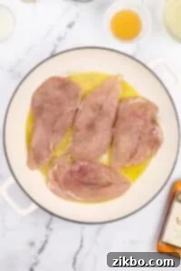 Chicken cutlets added to a skillet with oil and butter.
