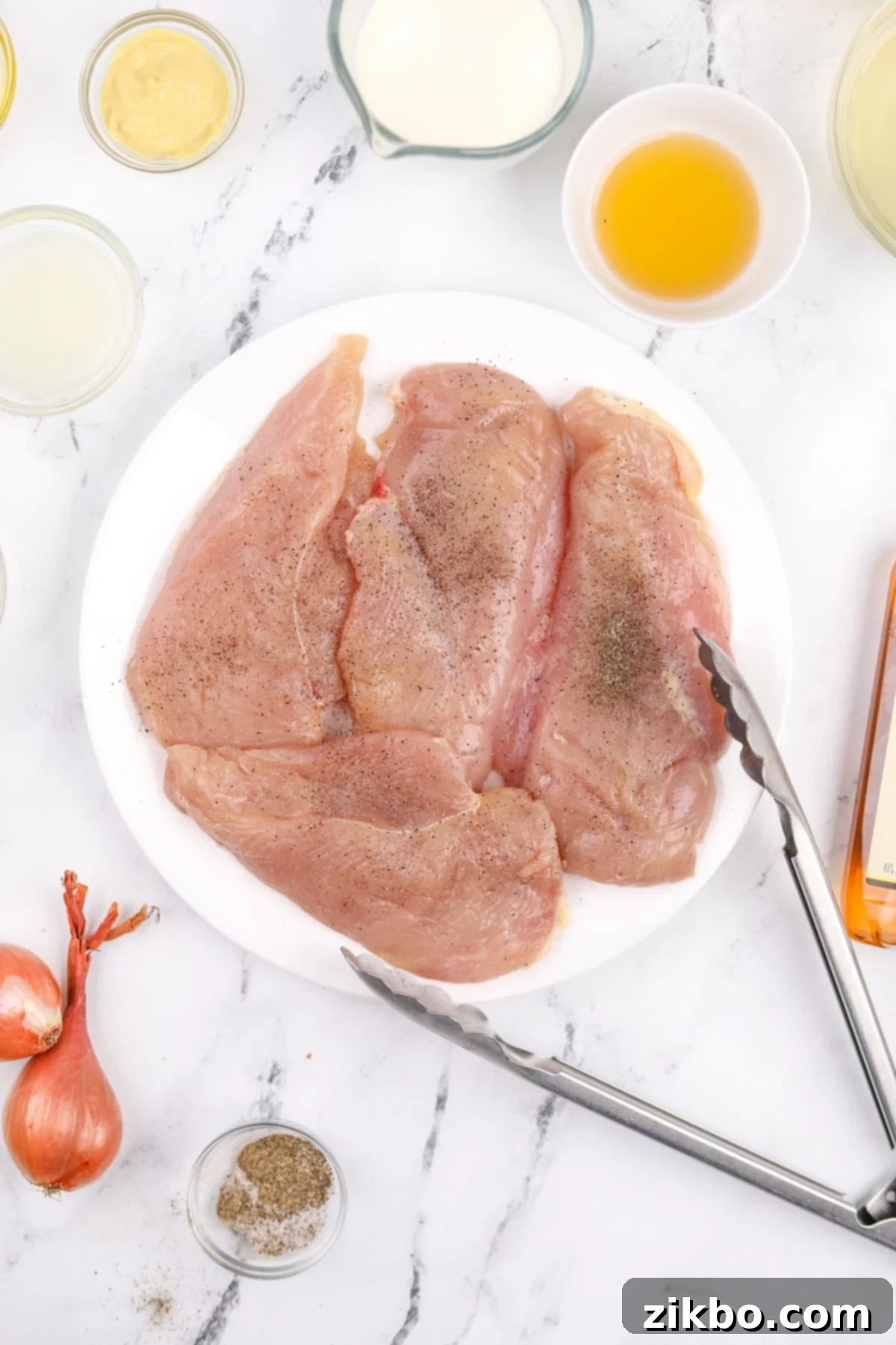 A white plate with chicken cutlets generously seasoned with salt and black pepper, ready for cooking.