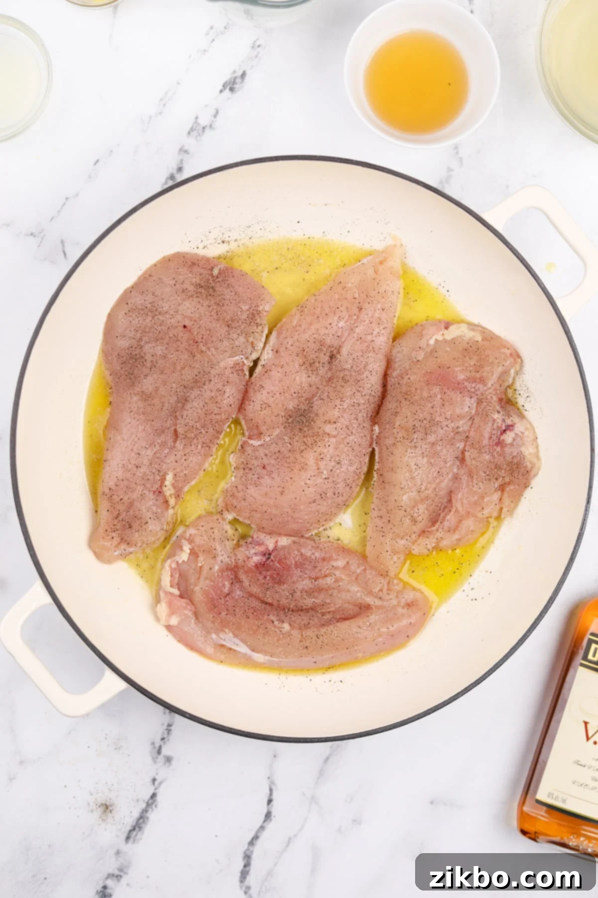 Seasoned chicken cutlets being carefully added to a hot skillet containing melted olive oil and butter.