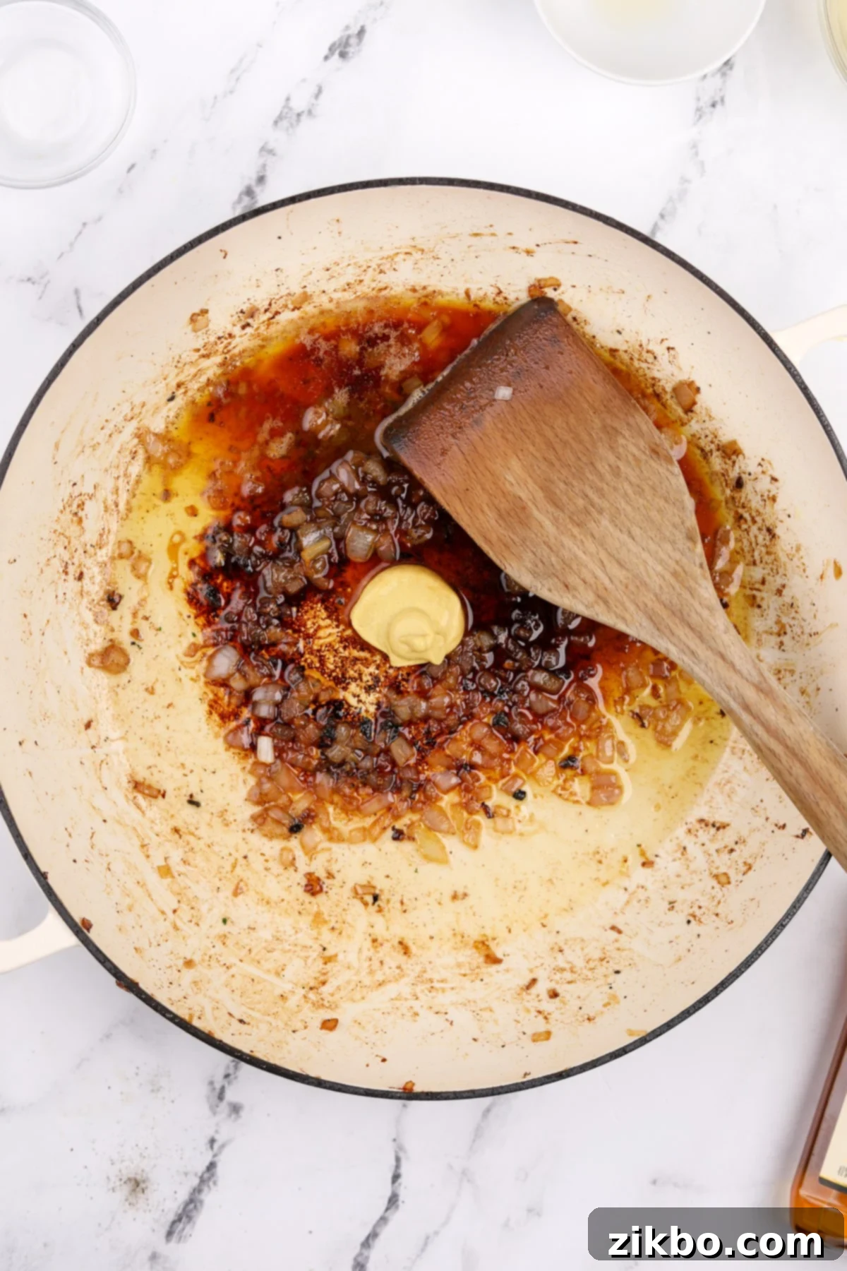 Dijon mustard, brandy, and lemon juice being added to the skillet with sautéed shallots, forming the aromatic base of the sauce.