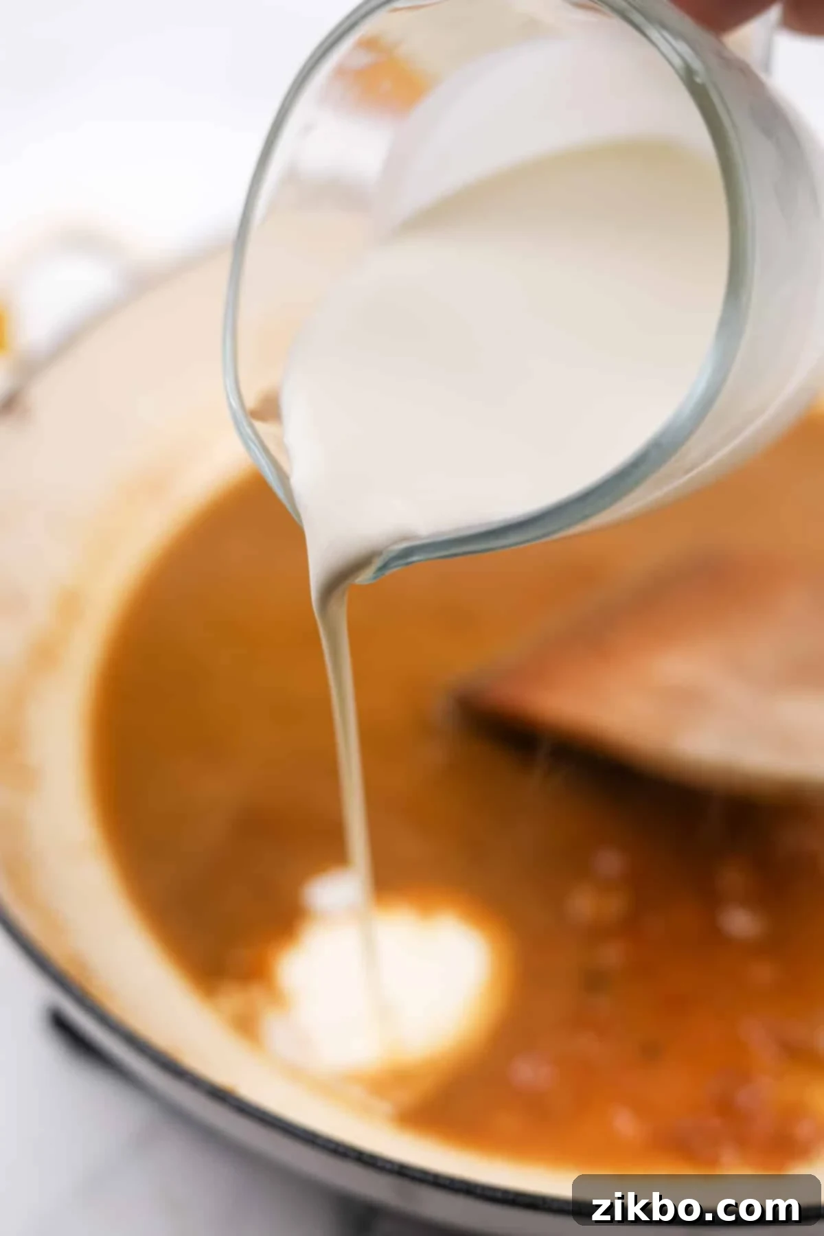 Rich heavy cream being poured into the skillet, ready to be stirred into the brandy and broth mixture to create a creamy pan sauce.