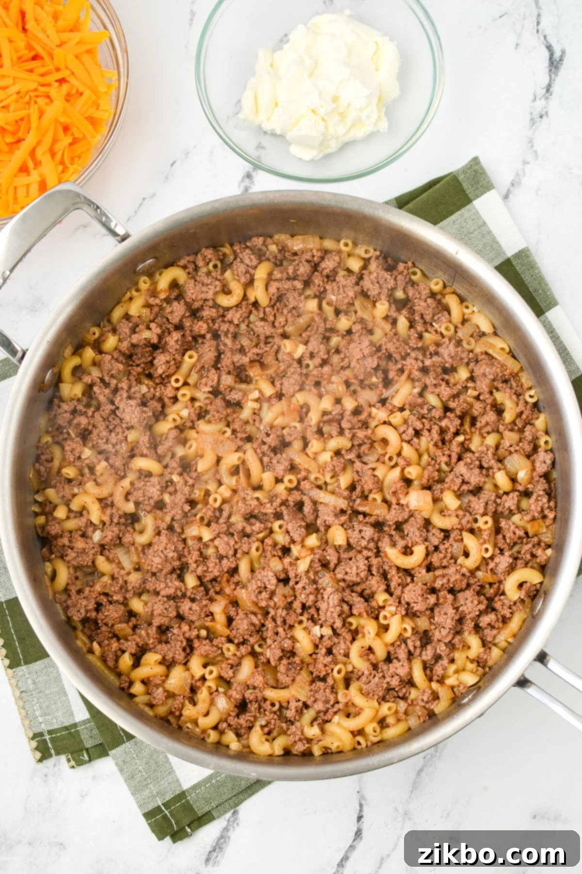 A skillet filled with ground beef and macaroni simmering in a creamy sauce.