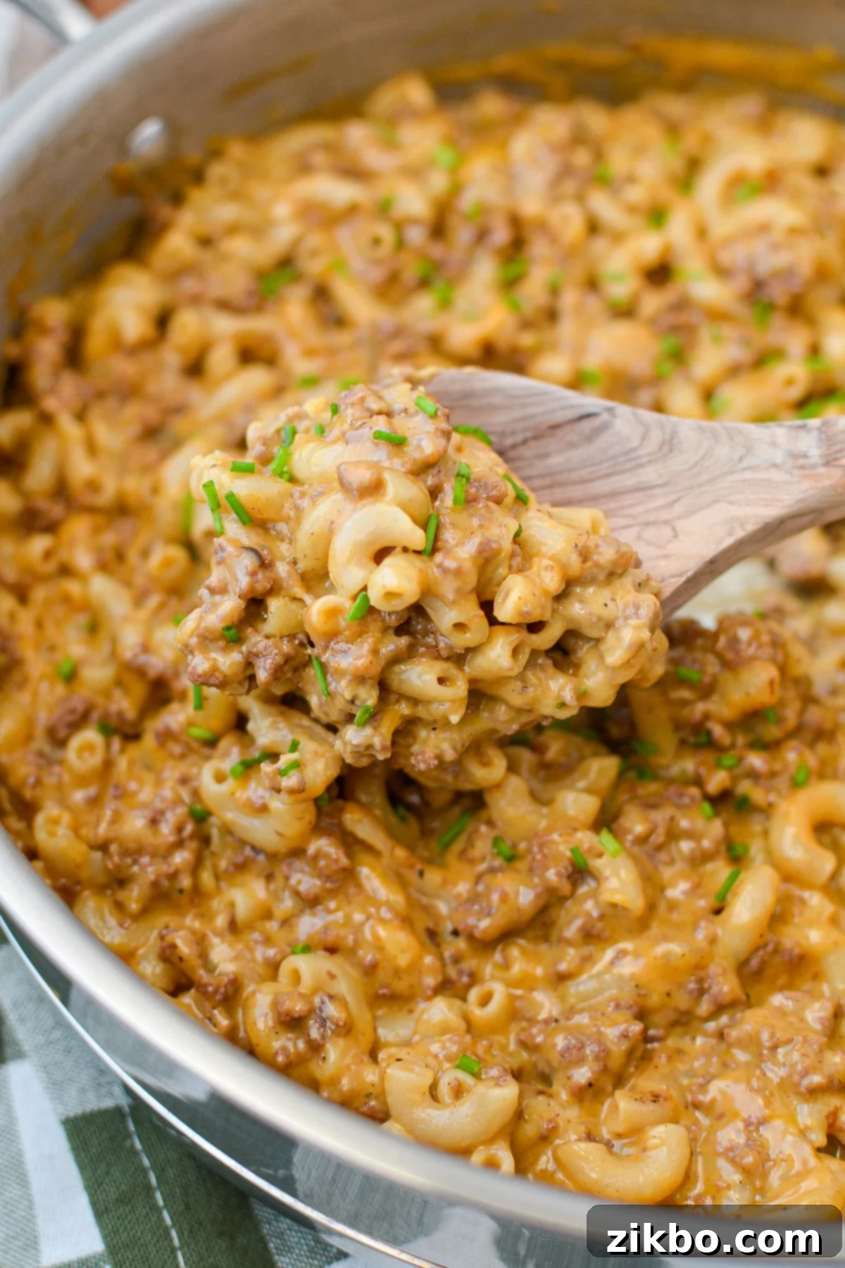 A wooden spoon scooping a generous portion of creamy hamburger helper from a skillet.