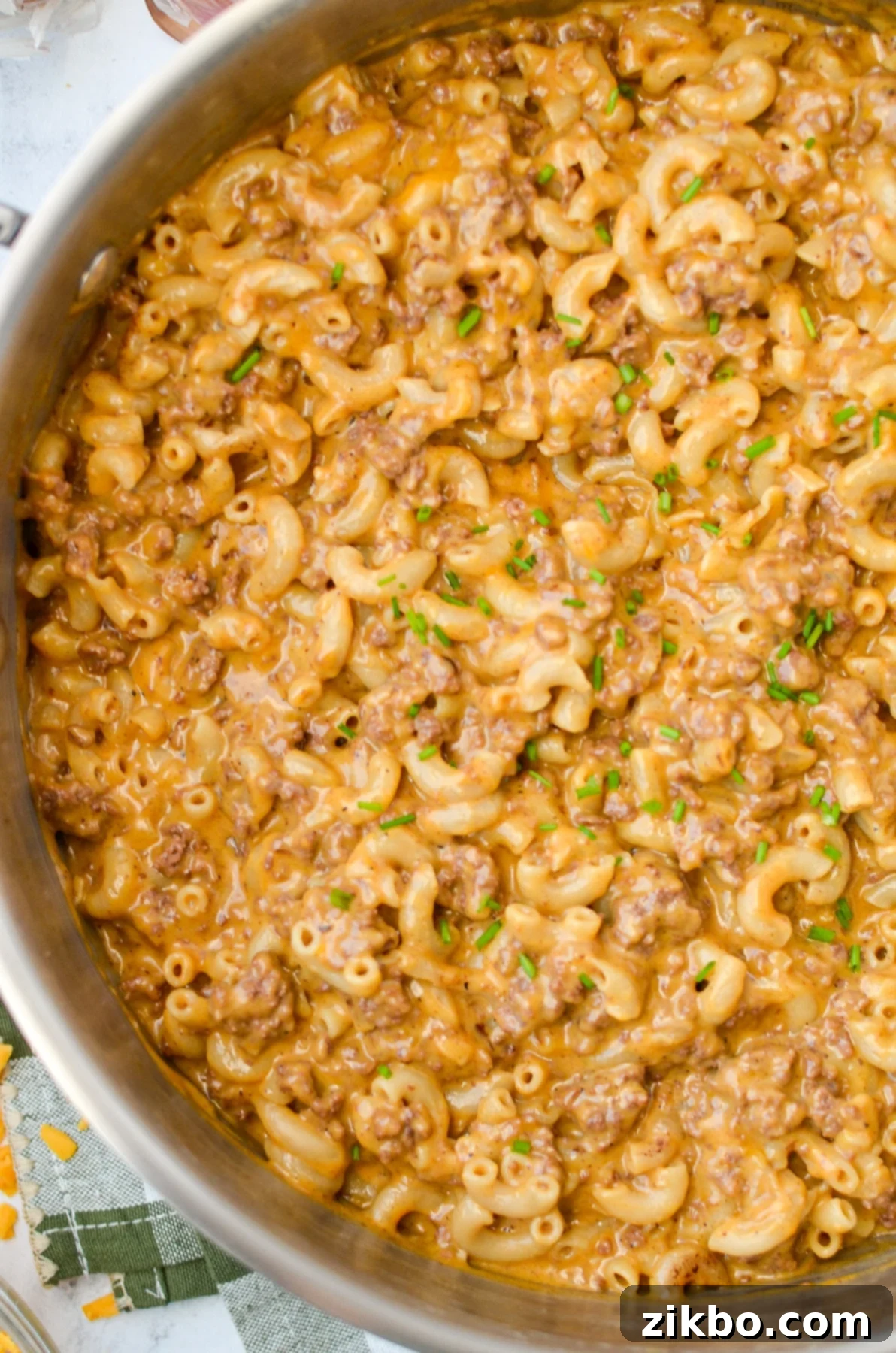 An overhead shot of a skillet with a creamy ground beef and pasta mixture, garnished with fresh herbs.