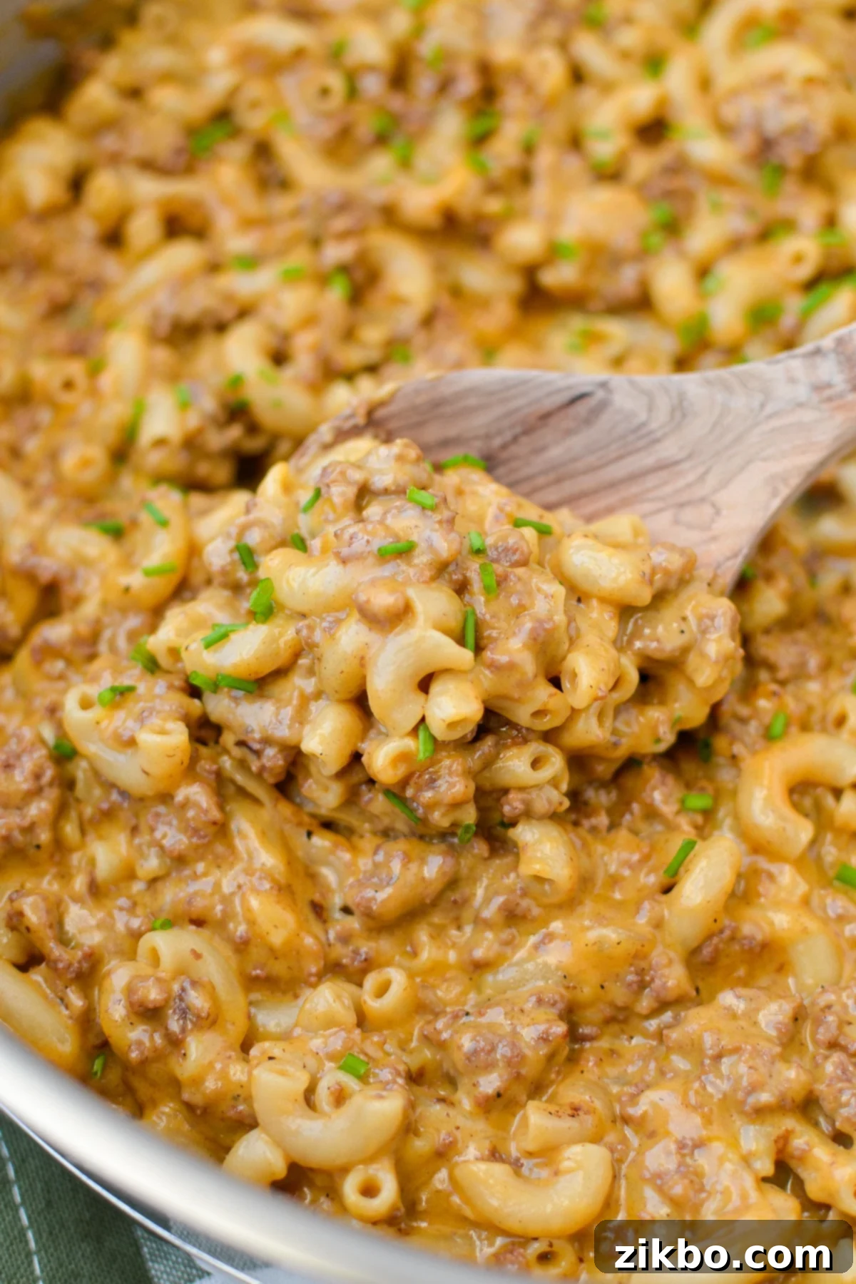 A wooden spoon scooping a portion of cheeseburger macaroni from a skillet, showing the creamy texture.