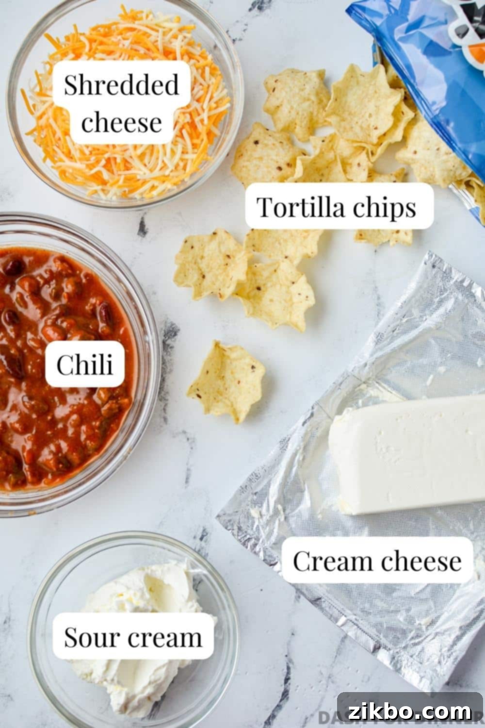 Easy Chili Cheese Dip 3 The ingredients needed to make chili cheese dip: cream cheese, sour cream, chili, and shredded cheese, arranged on a rustic surface.