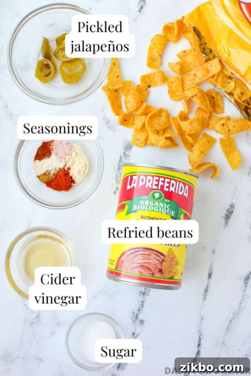Ultimate Homemade Fritos Bean Dip 3 The essential ingredients neatly arranged to make bean dip: canned refried beans, a selection of seasonings, cider vinegar, a pinch of sugar, and pickled jalapeno slices.