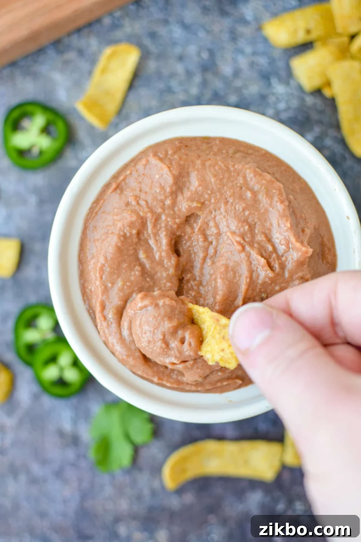 Ultimate Homemade Fritos Bean Dip 7 A hand dipping a Fritos corn chip into the creamy, homemade bean dip.