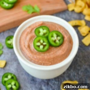 Ultimate Homemade Fritos Bean Dip 9 A bowl of creamy bean dip generously garnished with sliced jalapeños, ready for serving.