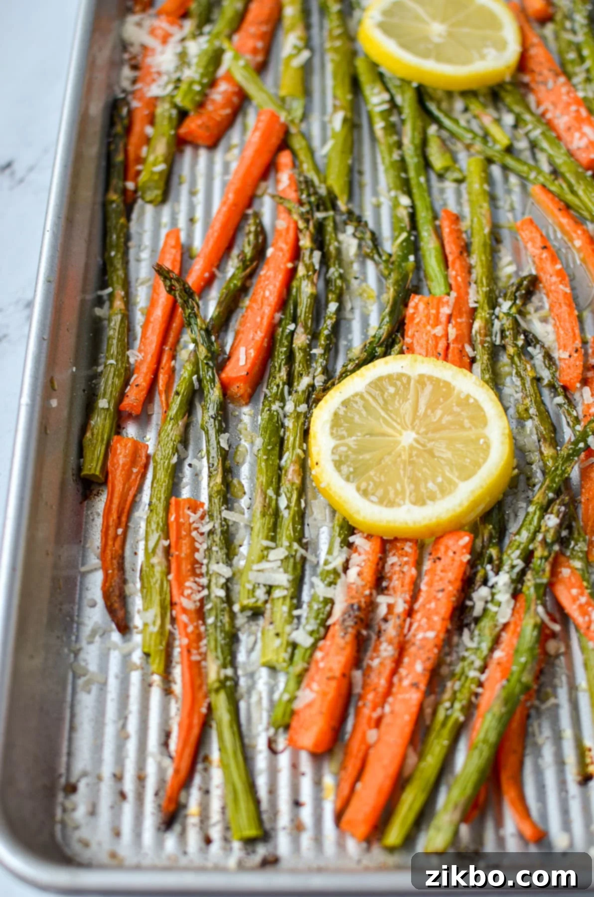 A sheet pan with perfectly roasted asparagus and carrots, beautifully garnished with fresh lemon slices.