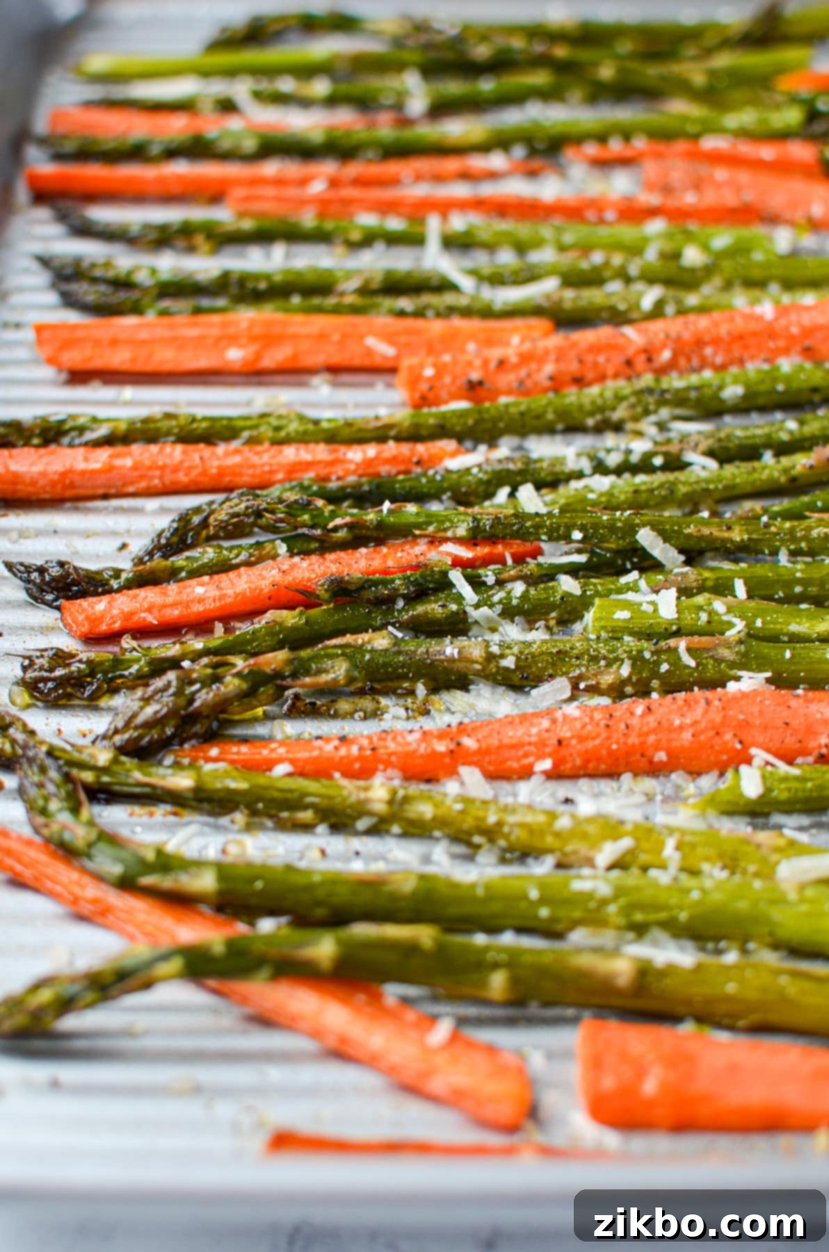 A sheet pan with glistening roasted asparagus and carrots, generously topped with grated parmesan cheese and ready to serve.