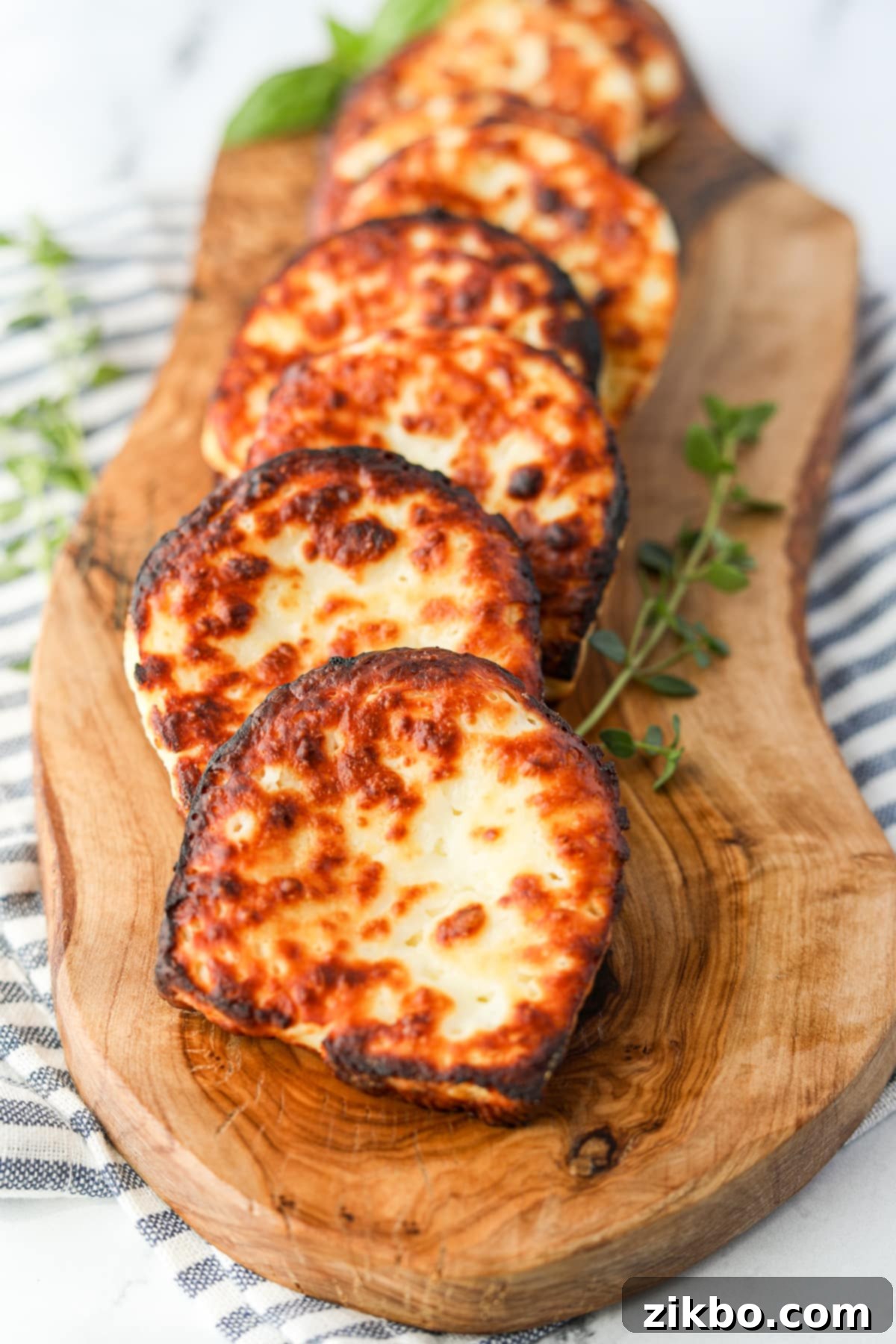 Slices of fried cheese on a wooden board, garnished with fresh herbs and a drizzle of honey.