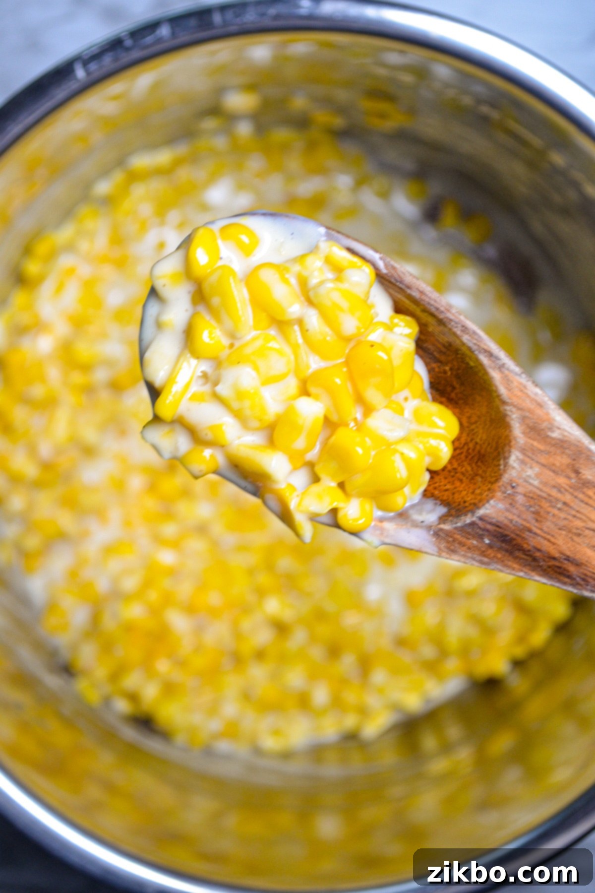 An Instant Pot filled with perfectly thickened creamy corn, with a wooden spoon serving a portion.