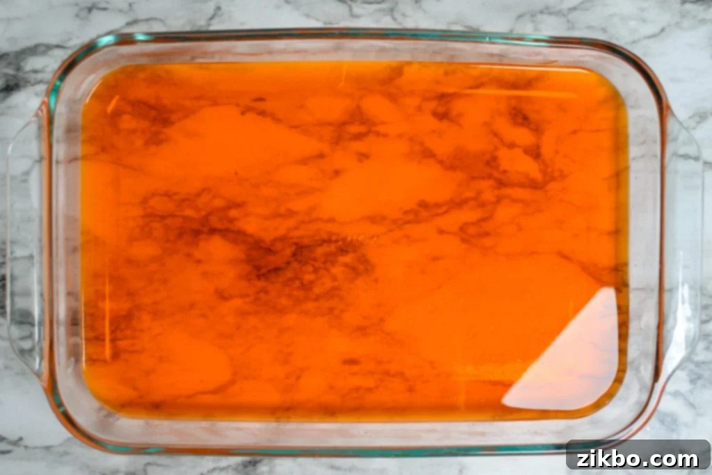 The bottom orange Jell-O layer perfectly set in a clear glass dish, ready for the next layer.