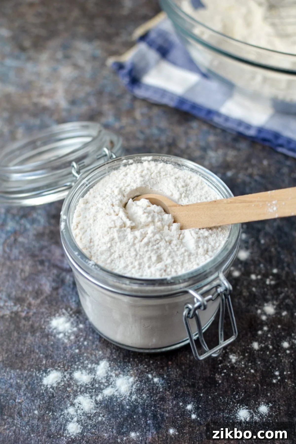 A small jar of homemade self-rising flour with a wooden spoon resting beside it.