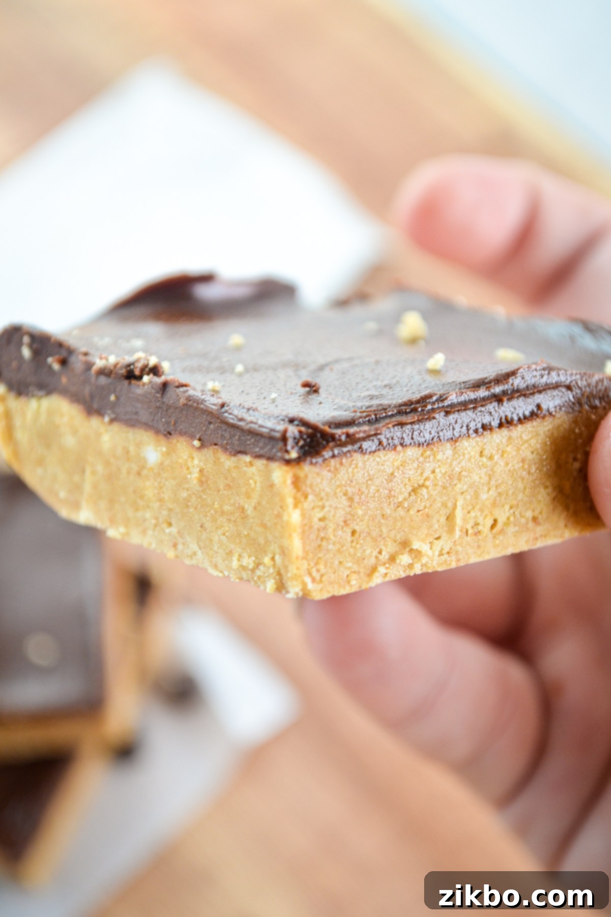 Holding up a single no bake peanut butter bar, showcasing its thick, inviting layers.