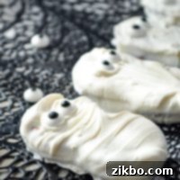 A nutter butter cookie, coated in white candy coating and dotted with two candy eyes, ready to be eaten.
