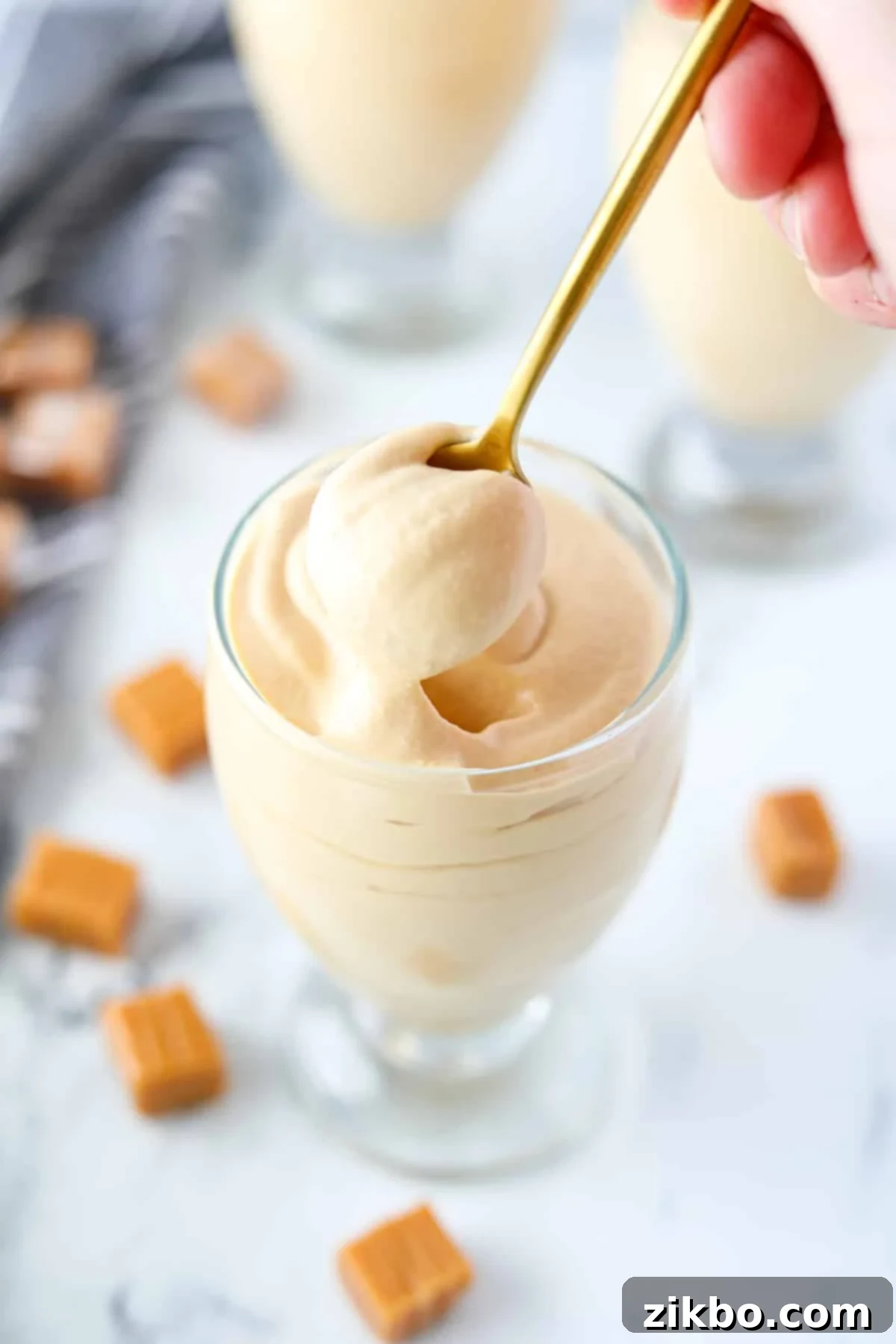 A gold spoon taking a portion of mousse from a glass jar, showcasing its smooth, creamy texture.