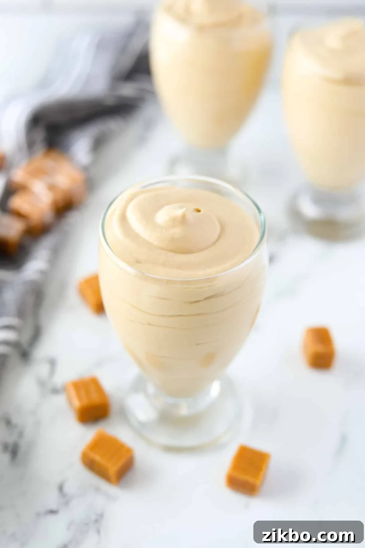 A beautifully presented jar of dulce de leche mousse, surrounded by unwrapped caramels, ready to be enjoyed.