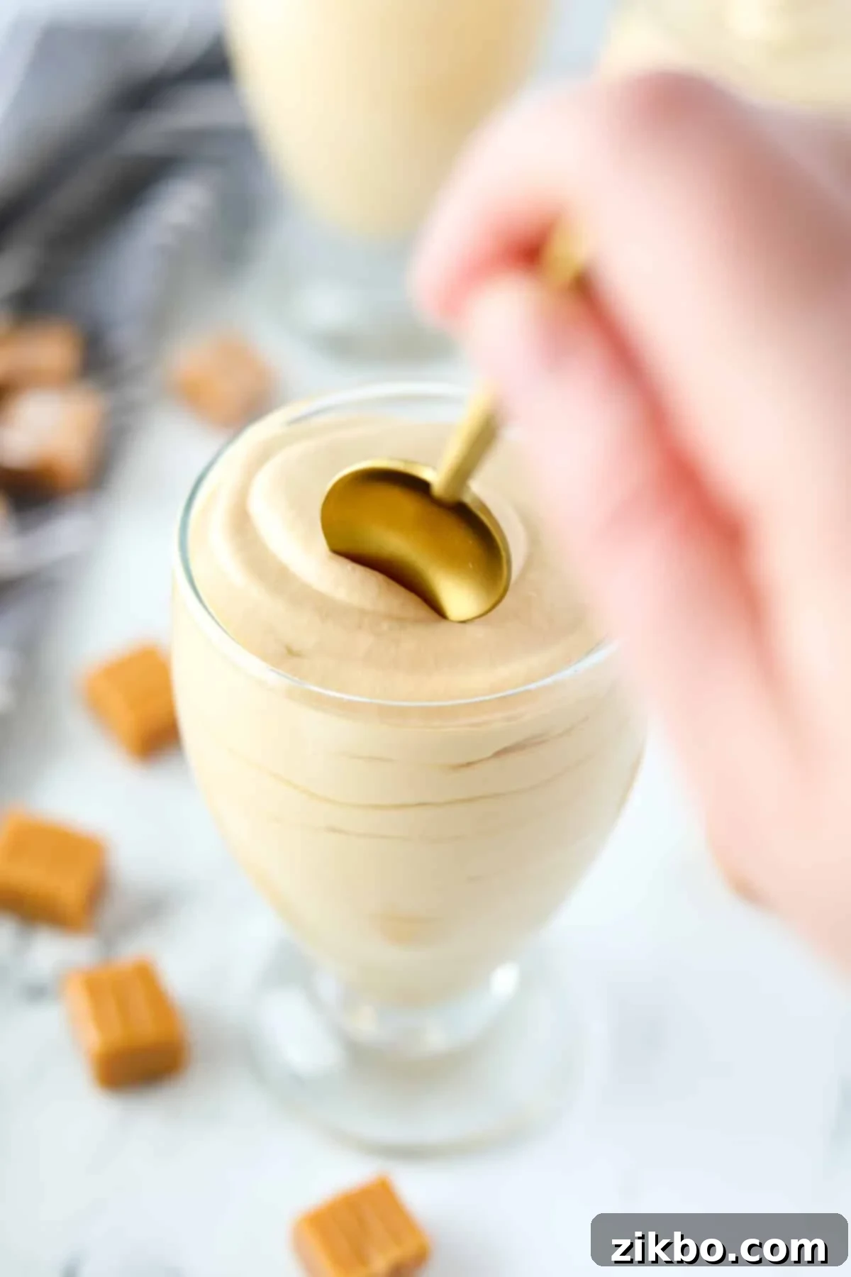 A gold spoon digging into a small amount of dulce de leche mousse in a dessert glass, highlighting its smooth texture.