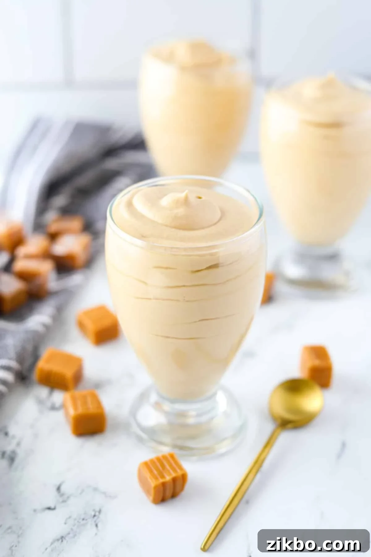 Multiple dessert glasses filled with creamy dulce de leche mousse, surrounded by shiny unwrapped caramels, inviting to be tasted.