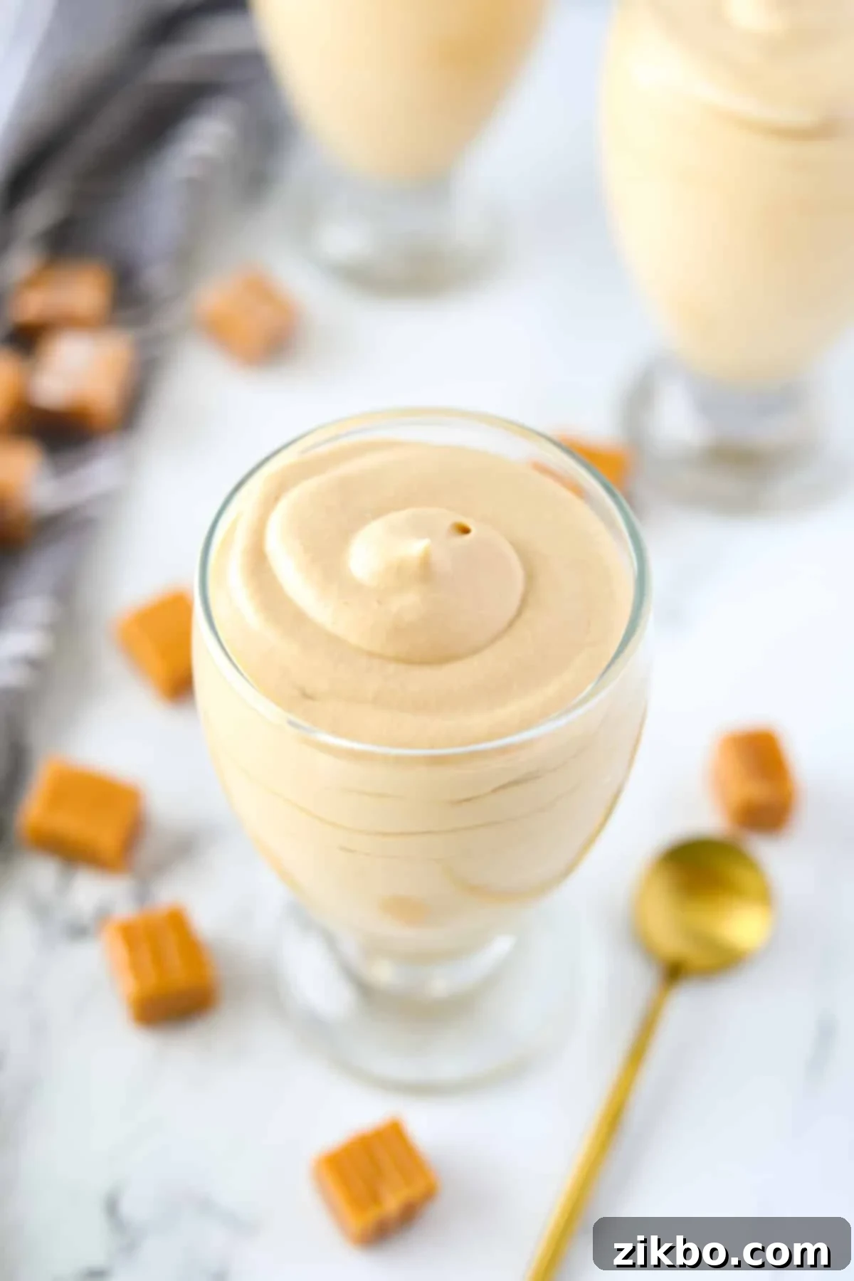A glass jar of creamy dulce de leche mousse with a elegant gold spoon resting on its side, ready for tasting.