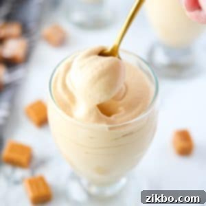 A gold spoon taking a portion of dulce de leche mousse from a glass jar, showing the creamy texture.