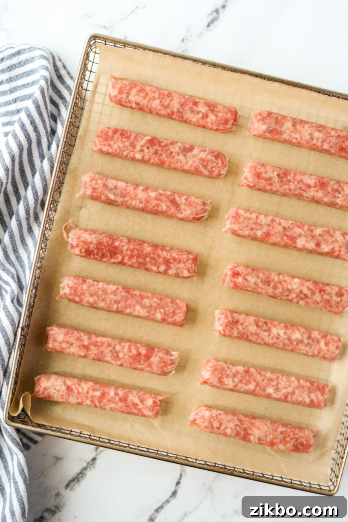 An air fryer tray filled with raw sausage links, evenly spaced.